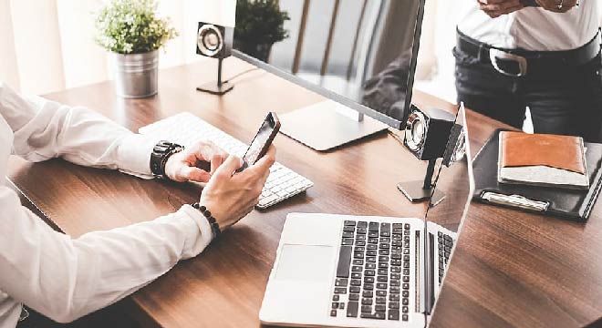 a desk with a computer, newspapers and a phone
