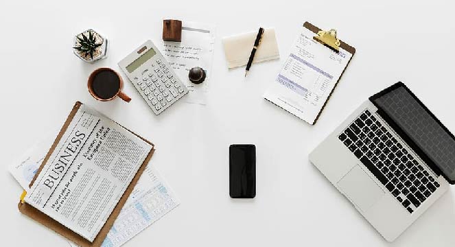 a desk with a computer, newspapers and a phone